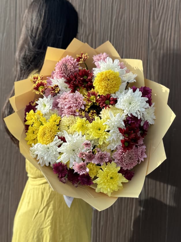 A vibrant bouquet of mixed yellow, white, pink, and burgundy asters