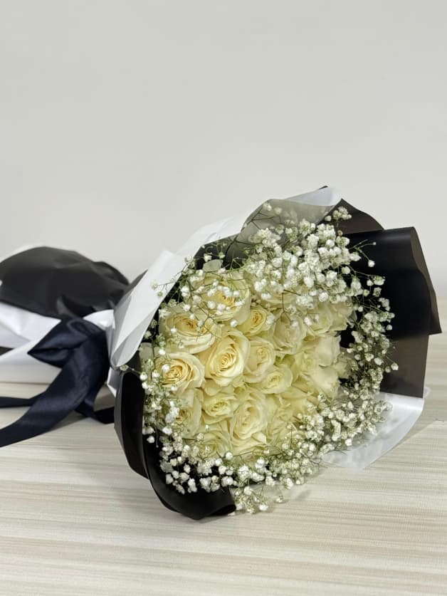 A chic bouquet of white roses and baby's breath in black wrapping