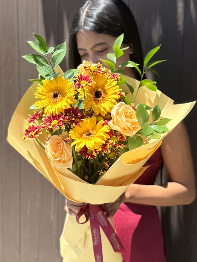 A cheerful bouquet of yellow gerberas, peach roses, and red spray chrysanthemums